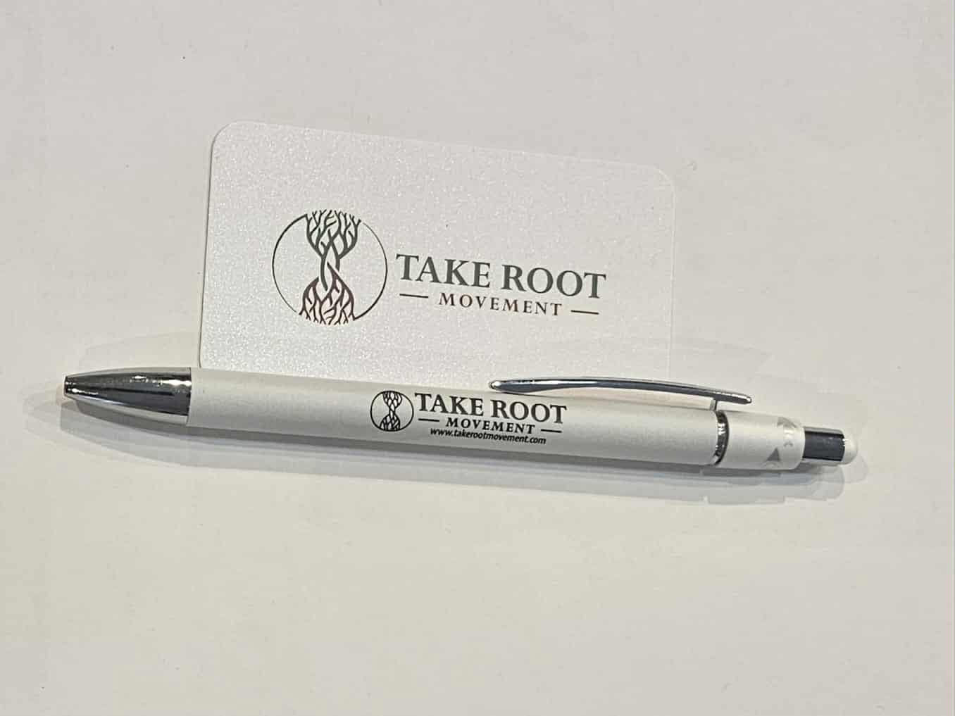 White click style pen with chrome accents featuring the Take Root Movement logo and website printed on the barrel, displayed on a light surface.