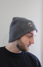 Side view of dark Grey beanie with hour glass logo with Take Root Movement next to it
