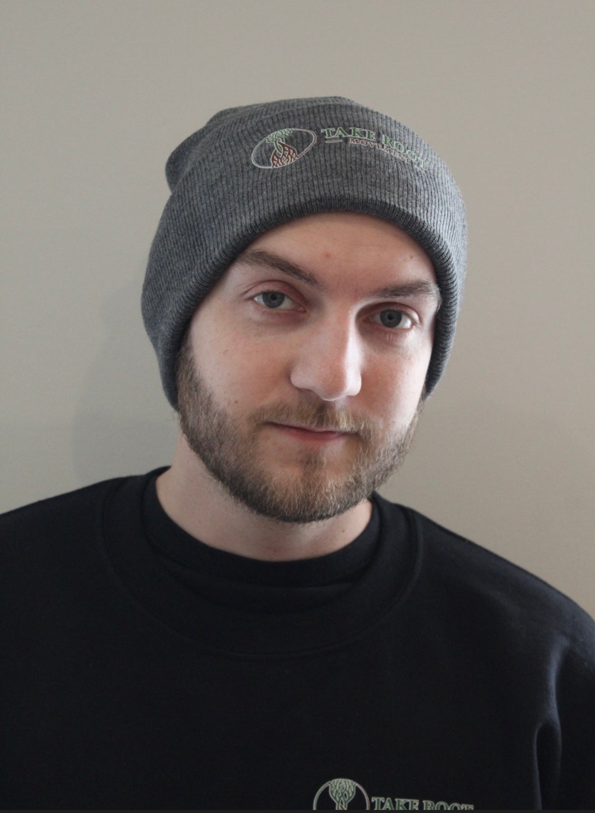 male wearing dark Grey beanie with hour glass logo with Take Root Movement next to it
