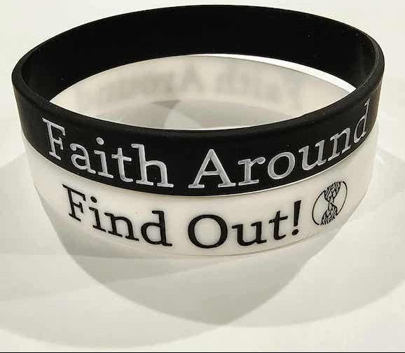 Close-up of stacked black and white ‘Faith Around Find Out’ Christian silicone wristbands featuring the Take Root Movement tree and roots logo.