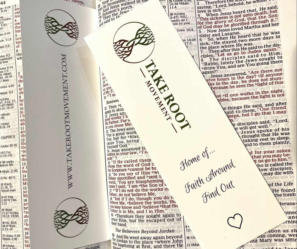 Two Take Root Movement Christian bookmarks placed inside an open Bible, featuring the intertwined tree and roots logo, ‘Faith Around Find Out’ message, and website on white cardstock.